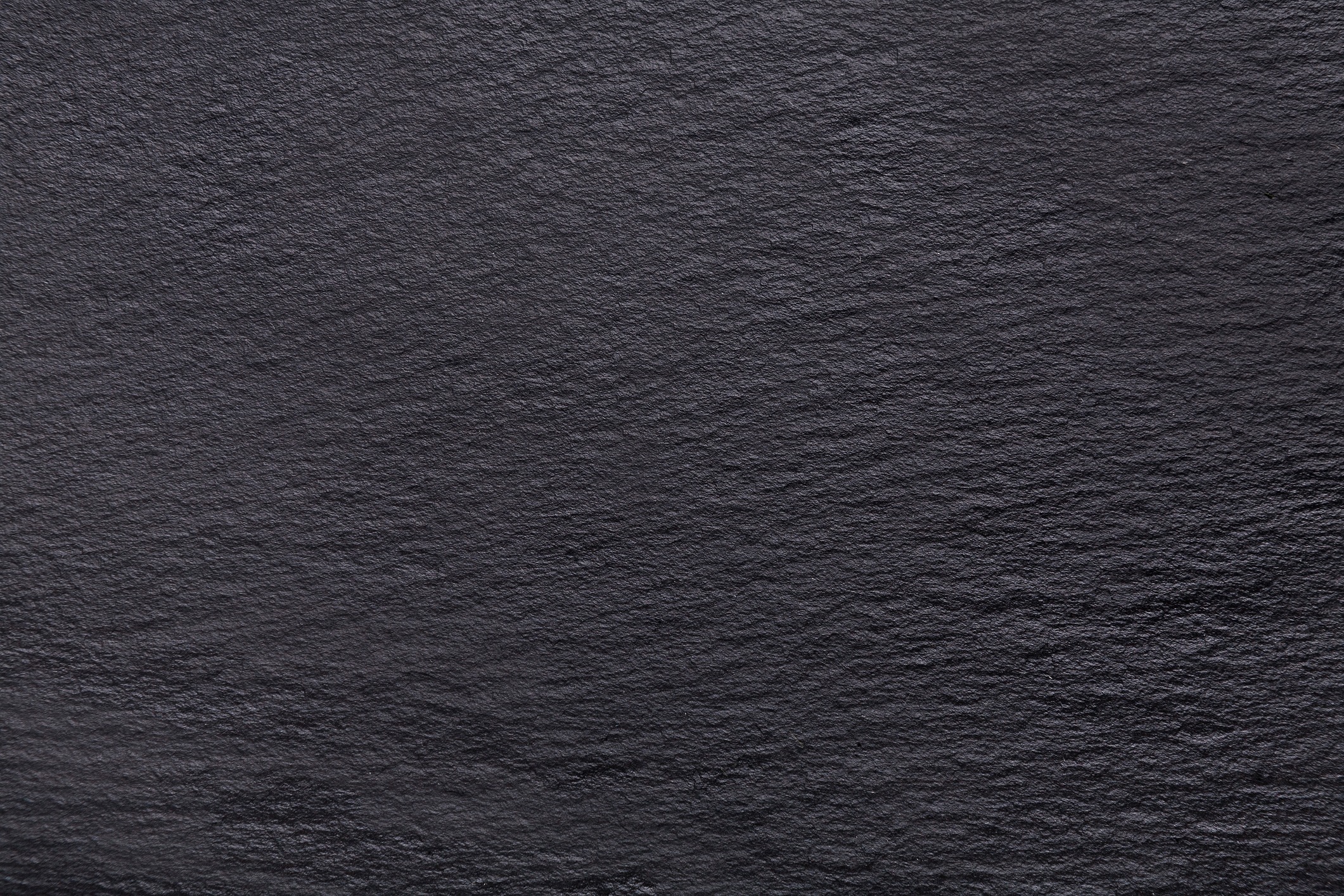 A close-up of a textured black surface, resembling slate. The image shows detailed patterns and subtle variations in color and texture.